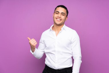 Asyalı yakışıklı adam mavi arka planda izole edilmiş bir şekilde bir ürün sunmak için kenarı işaret ediyor.