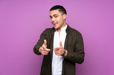 Asyalı yakışıklı bir adam mavi arka planda izole edilmiş. Önü işaret ediyor ve gülümsüyor.