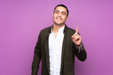 Asyalı yakışıklı adam mavi arka planda izole edilmiş ve en iyinin işareti olarak parmağını kaldırıyor.