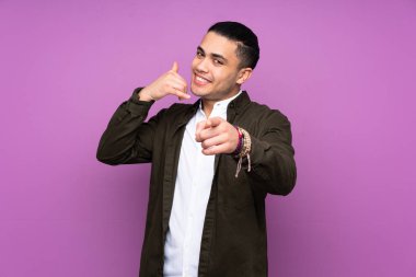 Asyalı yakışıklı adam mavi arka planda izole edilmiş telefon hareketi yapıyor ve ön tarafı işaret ediyor.