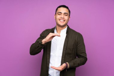 Asyalı yakışıklı bir adam mavi arka planda izole edilmiş. Avucunun içinde hayali bir ilan tutuyor.