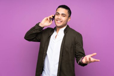 Asyalı yakışıklı adam mavi arka planda izole edilmiş. Cep telefonuyla biriyle sohbet ediyor.