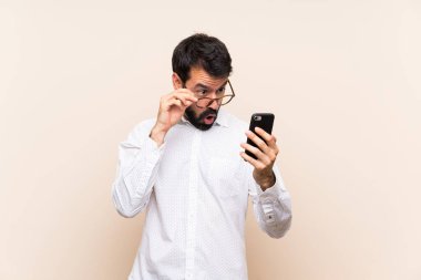 Sakallı genç adam cep telefonunu tutuyor ve şaşırıyor.