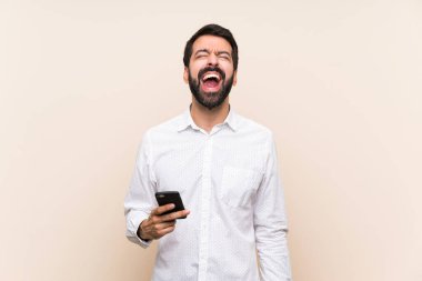 Elinde cep telefonu olan sakallı genç adam ağzı açık bağırıyor.