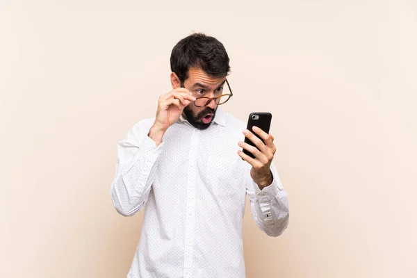 Joven Con Barba Sosteniendo Móvil Con Gafas Sorprendido —  Fotos de Stock