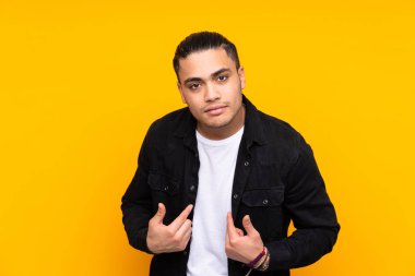 Asyalı yakışıklı adam sarı arka planda izole edilmiş. Durma hareketi yapıyor ve hayal kırıklığına uğruyor.