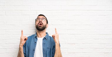 Beyaz tuğla duvarın üzerinde sakallı yakışıklı adam şaşırdı ve yukarı doğru işaret etti.