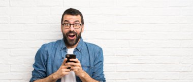 Beyaz tuğla duvarın üzerinde sakallı yakışıklı adam şaşırdı ve bir mesaj gönderiyor.