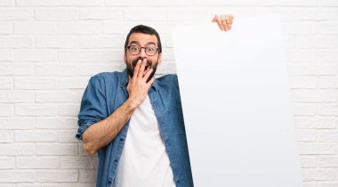 Boş bir pankart tutan beyaz tuğla duvar üzerinde sakallı yakışıklı adam