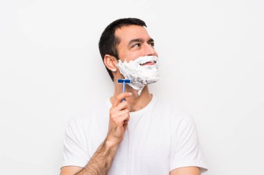 Sakalını beyaz arka planda kesen bir adam yukarı bakarken bir fikir düşünüyor.