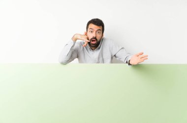 Sakallı, kocaman boş bir afiş tutan genç yakışıklı bir adam telefon hareketlerinde kuşkulanıyor.