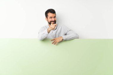 Sakallı, kocaman, boş bir levha tutan genç yakışıklı bir adam. Parmağını kendine güvenen bir ifadeyle sana doğrultuyor.