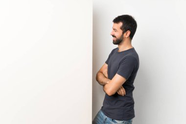 Sakallı, genç ve yakışıklı bir adam büyük boş bir levhayı yan pozisyonda tutuyor.