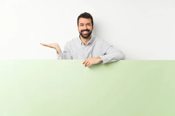 年轻英俊的男人 留着胡子 手里拿着一个大的绿色空标语牌 手上拿着一个想象中的复制空间 插入一个广告 — 图库照片