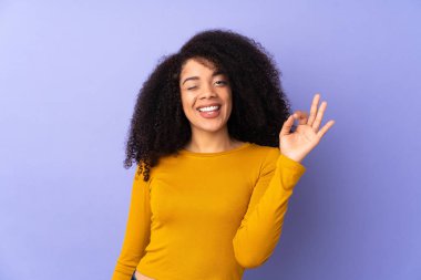 Mor arka planda izole edilmiş genç Afrikalı Amerikalı kadın parmaklarıyla tamam işareti gösteriyor.