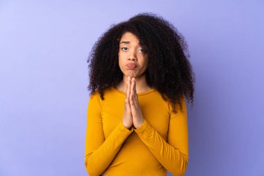 Mor arka planda izole edilmiş genç Afrikalı Amerikalı kadın avuç içlerini bir arada tutuyor. İnsan bir şey ister.