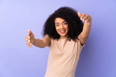 Genç Afro-Amerikalı kadın, mor arka planda izole edilmiş. Sunar ve davet eder.