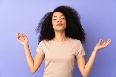 Genç Afrikalı Amerikalı kadın, mor arka planda zen pozuyla izole edilmiş.