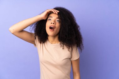 Mor arka planda izole edilmiş genç Afrikalı Amerikalı kadın yan tarafa bakarken sürpriz jest yapıyor.