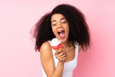 Genç Afrikalı Amerikalı kadın pembe arka planda izole edilmiş bir kornet dondurma tutuyor.