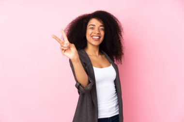 Genç Afro-Amerikalı kadın izole edilmiş arka planda gülümsüyor ve zafer işareti gösteriyor.