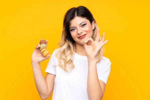 Menina Adolescente Isolada Fundo Amarelo Segurando Macarons Franceses Coloridos Convidando — Fotografia de Stock