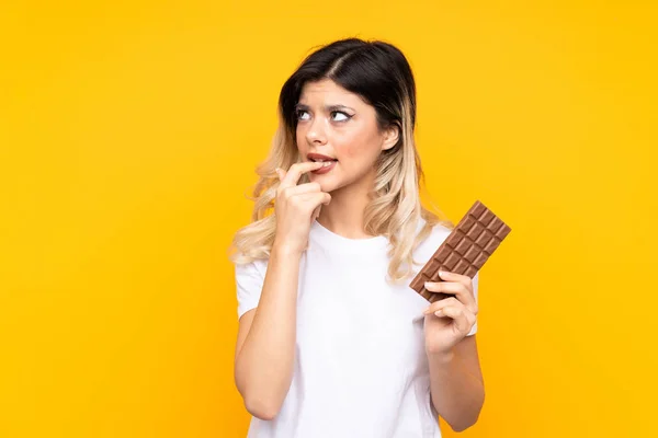 Teenager Dívka Izolované Žlutém Pozadí Čokoládovou Tabletu Mají Pochybnosti — Stock fotografie