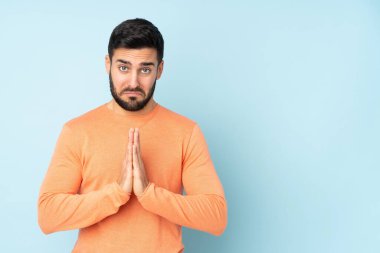 Beyaz tenli yakışıklı adam avucunu bir arada tutuyor. Kişi, izole edilmiş mavi bir arkaplan istiyor.