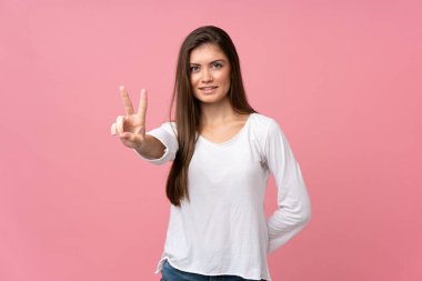 Soyutlanmış pembe arka planda genç bir kadın gülümsüyor ve zafer işareti gösteriyor