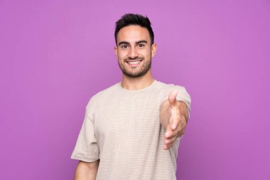 Soyutlanmış mor arka planda genç yakışıklı adam iyi bir anlaşma için el sıkışıyor.