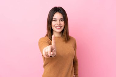 Soyutlanmış pembe arka planı olan genç bir kadın parmağını kaldırıyor ve gösteriyor.