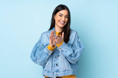 Mavi arka planda izole edilmiş genç beyaz kadın bir konferanstan sonra alkışlıyor.