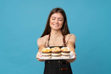 Mini kek tutan, izole edilmiş, mavi arka planı olan genç bir kadın.
