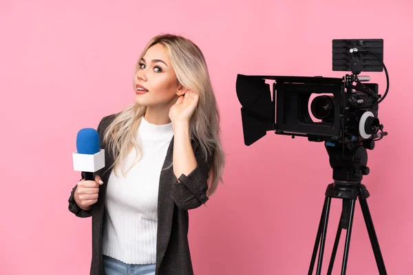 レポーター女性マイクを保持し 耳に手を置くことによって何かを聞く隔離されたピンクの背景の上にニュースを報告 — ストック写真