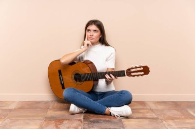 Young woman with guitar sitting on the floor thinking an idea