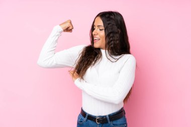 Soyutlanmış pembe arka planı olan genç bir kadın güçlü bir jest yapıyor.