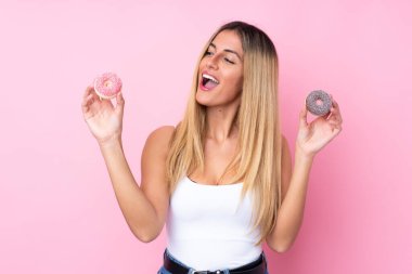Genç Uruguaylı kadın pembe arka planda mutlu bir ifadeyle donut tutuyor.