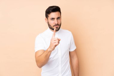 Beyaz tenli yakışıklı adam bej arka planda izole edilmiş hayal kırıklığına uğramış ve ön tarafı işaret ediyor.