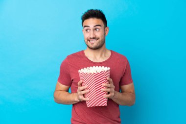 Soyutlanmış mavi arka planda genç yakışıklı bir adam elinde koca bir kova patlamış mısır tutuyor.