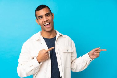 Genç Afro-Amerikalı adam mavi arka planda şaşırmış ve işaret ediyor.