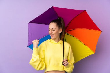 Mor duvarın üzerinde şemsiyesini tutan esmer bir kadın zaferi kutluyor.