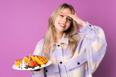 Mor arka planda izole edilmiş waffle 'lar tutan genç Rus kız bir şeye bakmak için çok uzaklara bakıyor.