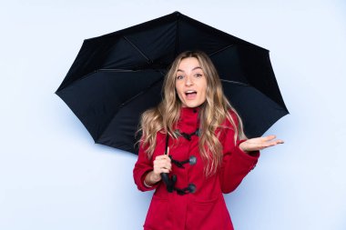 Kışlık paltolu ve yüzünde şok ifadesi olan bir şemsiye tutan genç bir kadın.