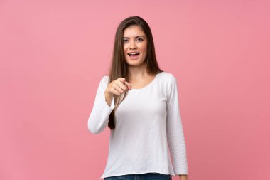 Soyutlanmış pembe arka planı olan genç bir kadın şaşırmış ve ön tarafı işaret ediyor.