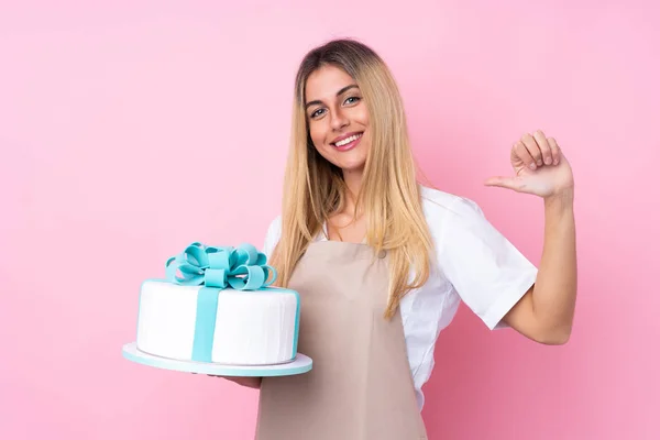 Young Uruguayan pastry woman with a big cake over isolated pink background proud and self-satisfied
