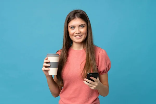 Giovane Donna Sfondo Blu Isolato Possesso Caffè Portare Cellulare — Foto Stock