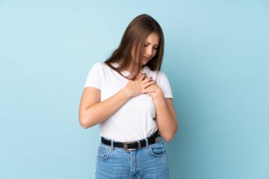 Kafkasyalı genç bir kız mavi arka planda izole edilmiş, kalbinde ağrı var.