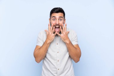 Sakallı, mavi arka planda, yüzünde sürpriz bir ifade olan yakışıklı bir genç.