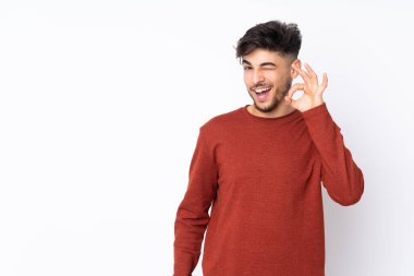 İzole edilmiş arka planda yaşayan Arap yakışıklı adam parmaklarıyla tamam işareti gösteriyor.