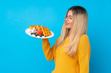 İzole edilmiş arka planda mutlu bir ifadeyle waffle tutan genç bir kadın.